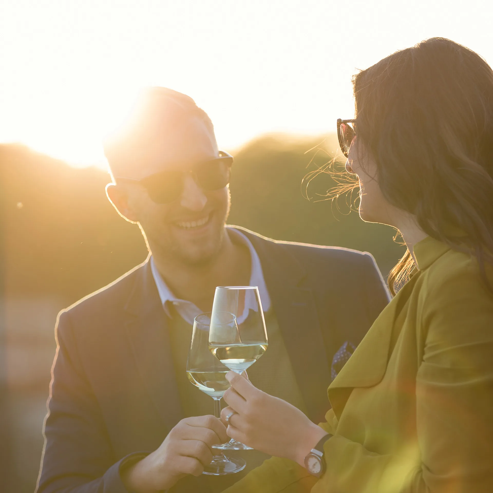 Stylish, happy couple toasting with wine on the rooftop as the sun sets